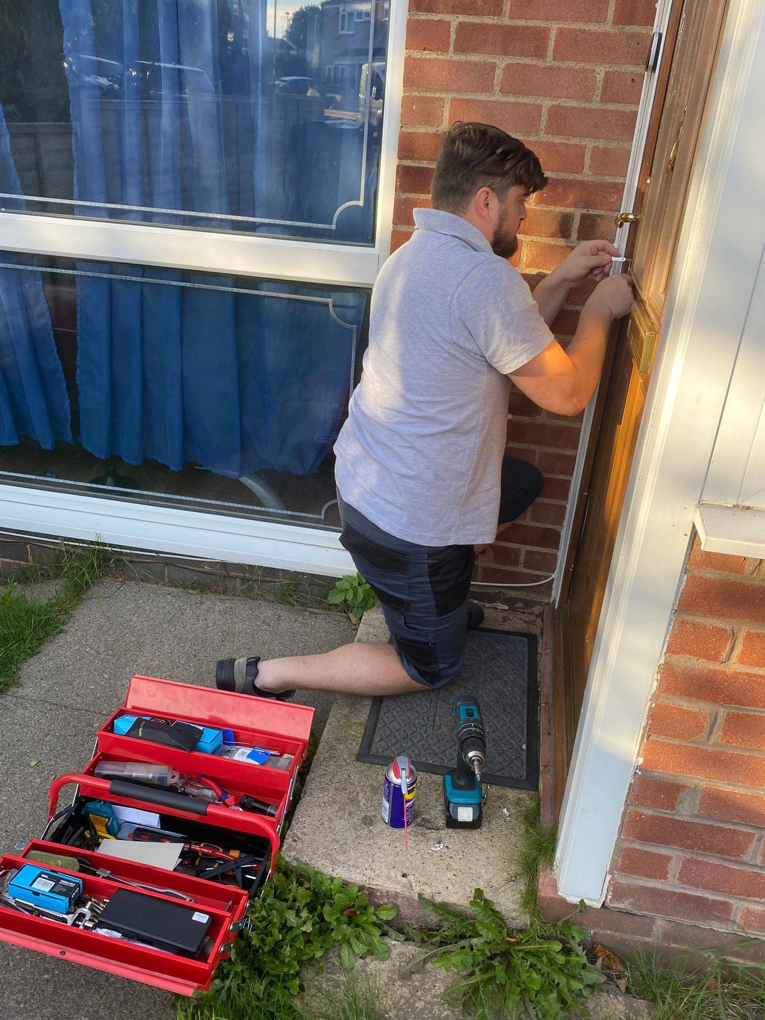 Professional Locksmith kneeling at a front door repairing the lock with tools and toolbox